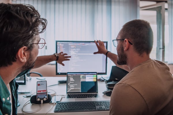 Two tech employees gesturing at a computer with code_608681961